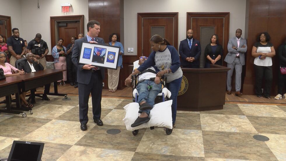 Montgomery DA Daryl Bailey presents a framed Officer of the Month award to MPD Officer Carlos...